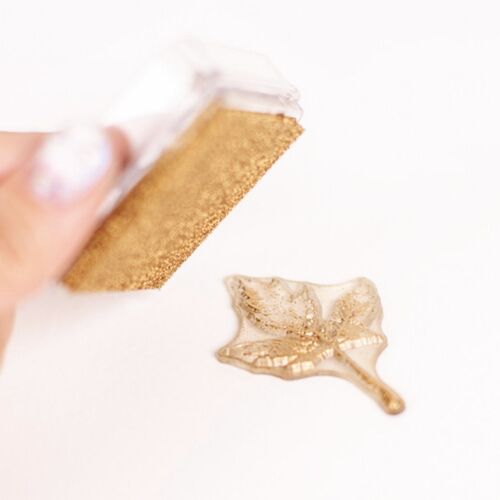 A close-up of a metallic shimmer stamp pad in gold, with a glistening gold stamp impression on a white surface, showcasing its radiant finish.