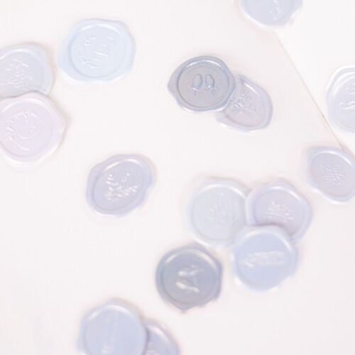 Translucent, embossed wax seal stickers with floral and script designs, arranged on a white surface to showcase their delicate details.