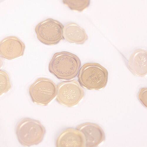 Gold and beige wax seal stickers with embossed floral and text designs are scattered on a white surface, showcasing their elegance.