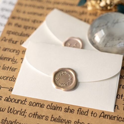 Close-up of white sealing wax stickers with embossed floral and text designs, arranged on a textured background with a glass marble and paper accents.
