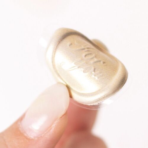 A close-up of a gold sealing wax sticker with embossed floral and text details, held between fingers against a plain white background.