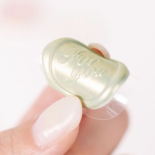 A close-up of a single iridescent sealing wax sticker, showcasing its glossy finish and intricate embossed design, held between fingers.
