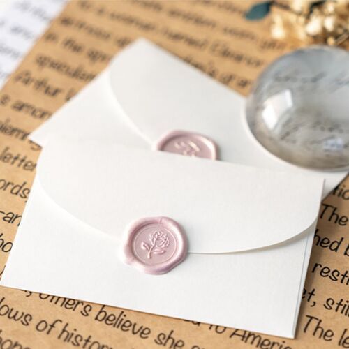 Two white sealing wax stickers with embossed floral and word designs are neatly placed on a textured background, highlighting their elegant details.