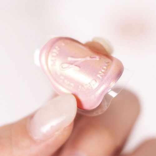A close-up of a pink sealing wax sticker with embossed floral and text details, held between fingers against a soft, neutral background.
