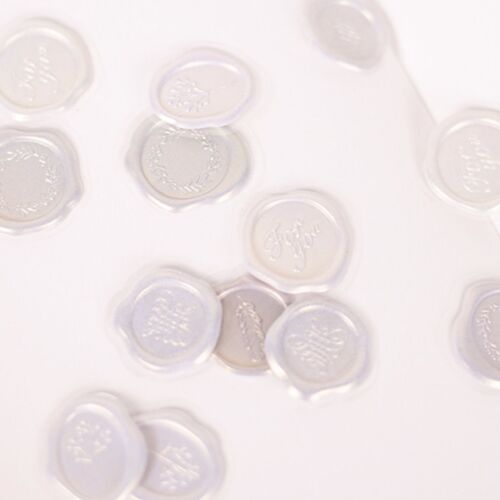 Clear, glossy sealing wax stickers with embossed floral and text designs are scattered on a white surface, showcasing their elegant details.