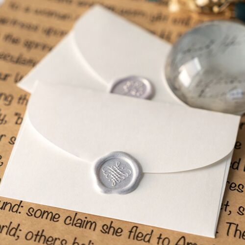 Two white sealing wax stickers with embossed floral and word designs are displayed on a background of handwritten letter paper and a decorative marble paperweight.