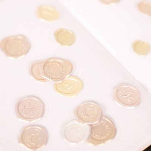 Close-up of self-adhesive sealing wax stickers in soft pastel shades with embossed floral and word designs on a white surface.
