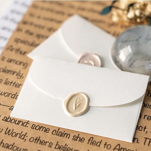 Two white self-adhesive sealing wax stickers with embossed floral and word designs are prominently displayed on a background of handwritten text and decorative elements.