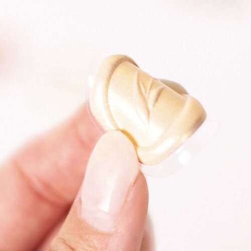 A close-up of a gold-colored sealing wax sticker with embossed floral design, held between fingers against a bright, neutral background.