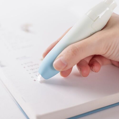 The correction tape features a soft pastel gradient in light blue and white, shown being smoothly applied over paper in a close-up shot.