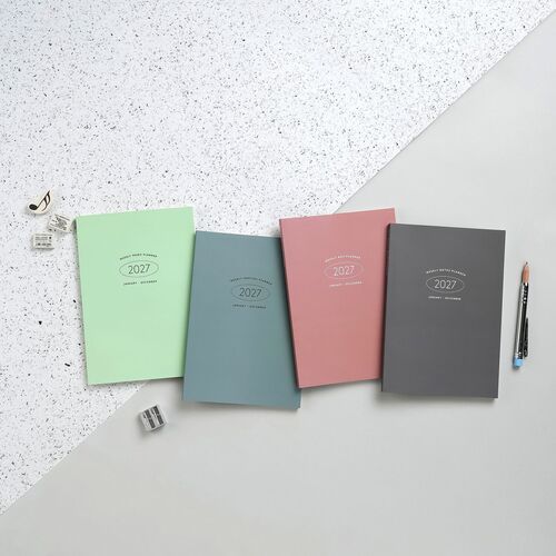 Colorful planners in pastel shades—green, blue, pink, and gray—are neatly arranged on a split-textured surface, showcasing their sleek covers.