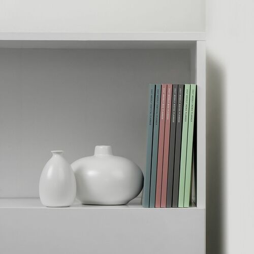 The image showcases a neat collection of colorful 2027 weekly planners standing upright on a minimalist white shelf, accompanied by two smooth, white ceramic vases.