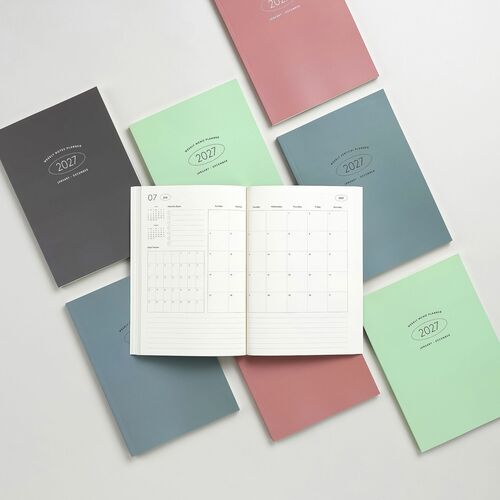 Multiple 2027 planners in pastel shades, open to reveal clean, organized weekly layouts with distinct styles and high-quality paper.
