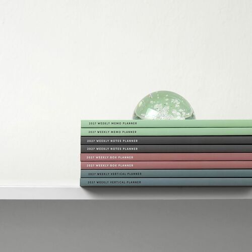 Stacked planners in pastel shades with clear, legible labels, arranged neatly against a minimalist white background, emphasizing organization and color variety.