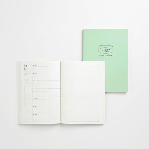 An open 2027 weekly planner with minimalist white pages displaying a weekly layout, placed beside a mint green cover on a clean white surface.