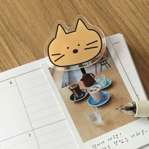 A tan cat clip rests on a book and photo page, adding a small illustrated accent to reading materials.