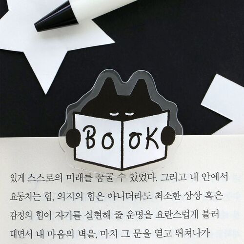 The Smile clip lies between open books, showing its use as a bright decorative bookmark.