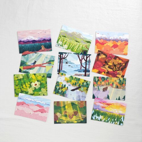 Twelve illustrated postcard designs are arranged together, showing the collection’s range of mountains, forests, wildlife, flowers, and seasonal scenery.