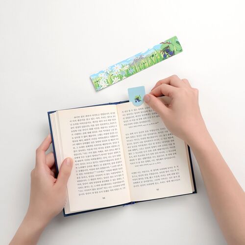 The bookmark’s colorful floral and berry landscape is shown above an open book with the pop-out tab in use.