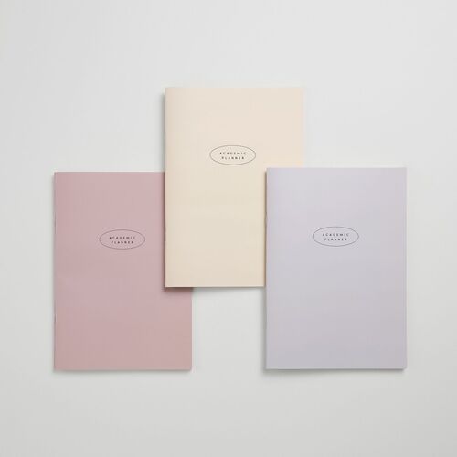 All three cover colors are arranged with a blank sample page, showing their compact soft-cover format and centered Academic Planner mark.