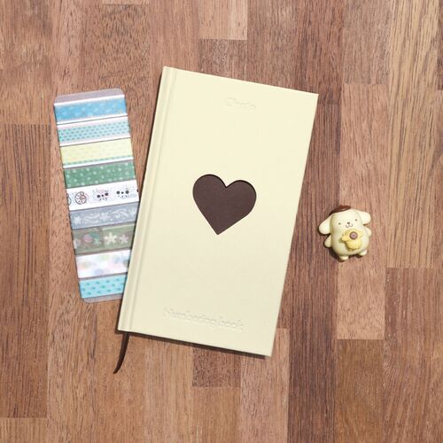 Butter is shown on a wood surface with stationery, revealing the soft cream cover and dark heart window.