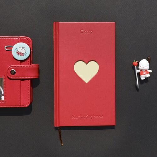 An Apple journal rests beside a planner, showing its bold cover color and centered heart cutout.