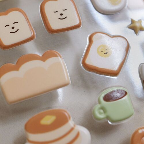 This detail highlights the smiling toast, fried egg toast, cream-colored bread, green coffee cup, and chocolate dessert designs.