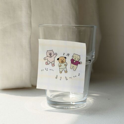 Three colorful characters decorate a small card displayed beside a clear glass in bright window light.