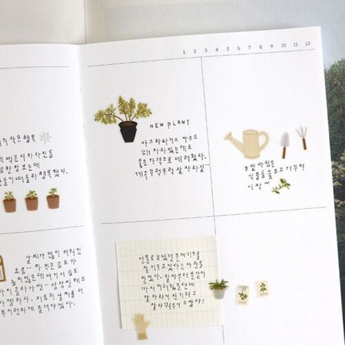 Several plant and gardening designs are arranged across an open journal, including potted greenery, a watering can, and small tools.