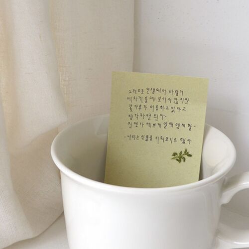 A pale green note card sits inside a white cup, finished with a small leafy sticker near the bottom.