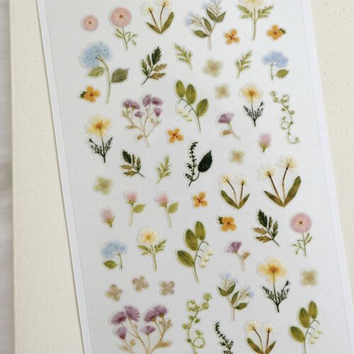 The close crop highlights varied floral shapes, leafy stems, tiny blossoms, and the soft pale edging around each sticker.