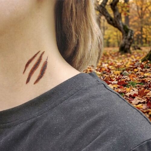 A long Wound Effect tattoo sits across the wrist, showing textured dark shading and red edges against autumn leaves.