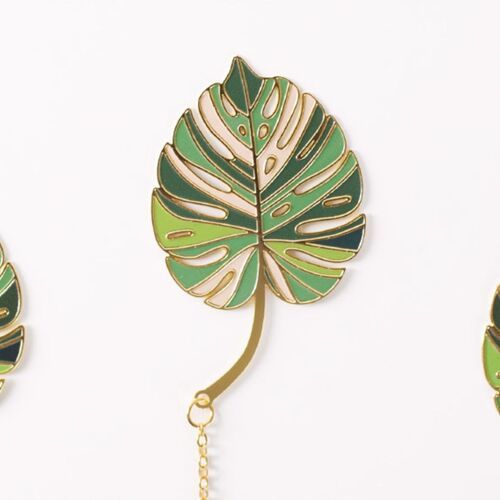 A hand slides the Monstera Leaf bookmark between open pages for a clear view of its everyday use.