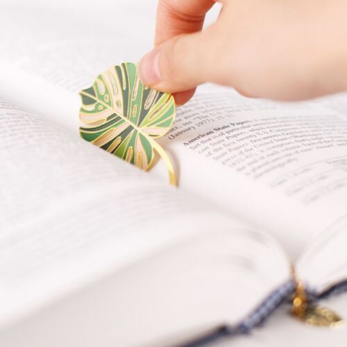 Monstera Leaf lies across an open book, with the slim chain trailing neatly across the printed page.
