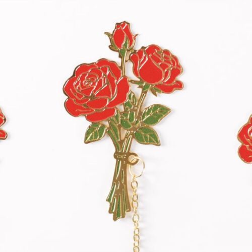 Rose lies across printed pages while its delicate chain stretches outward to the matching charm.