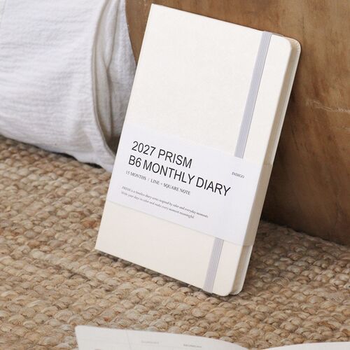 The Cloud planner stands upright on a soft surface, showing its pale cover, rounded corners, and light elastic band.