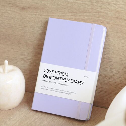 Lilac lies open beside a small white object, showing the color and rounded edge of the closed planner.
