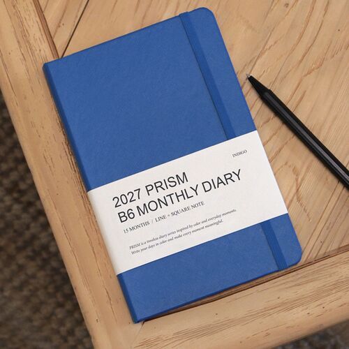 Classic Blue rests on a wooden surface beside a pen, emphasizing the planner’s compact desk-friendly format.