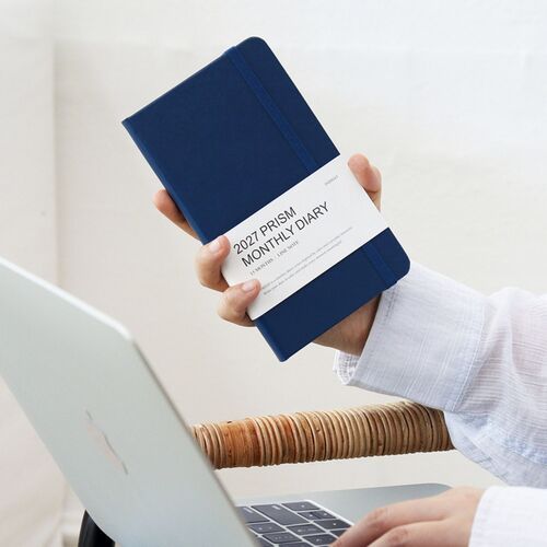 A Classic Blue planner is held upright, showing its compact slim format and white product band against a clean background.