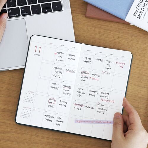 An open monthly spread shows spacious date boxes filled with handwritten appointments, reminders, and colorful planning marks.