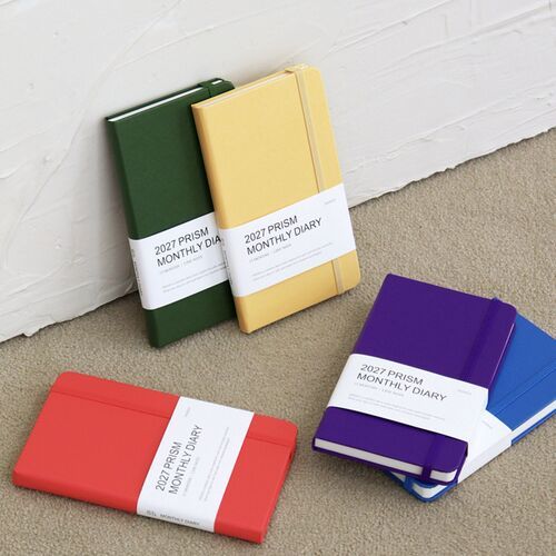 A Classic Blue planner is lifted from a stack, showing its flexible elastic closure and compact portable shape.