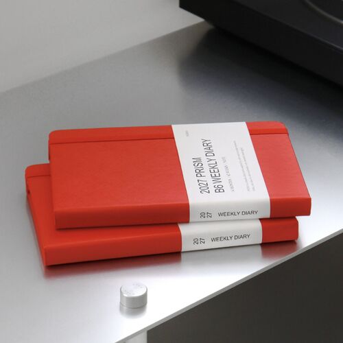 Two Tomato Red planners are stacked on a reflective surface, showing the sturdy covers and compact thickness.