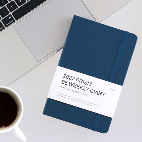 A Classic Blue planner rests beside a laptop and coffee, presenting its compact size in a desk setting.