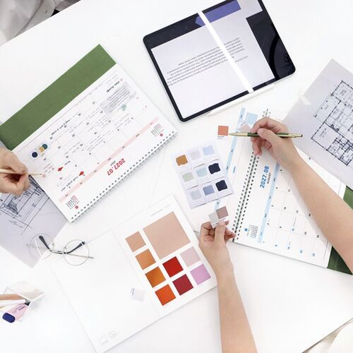 An overhead planning scene shows the calendar open among design papers, color samples, and writing tools.