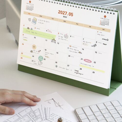 A hand writes directly into a monthly grid, showing room for appointments, notes, and schedule details.