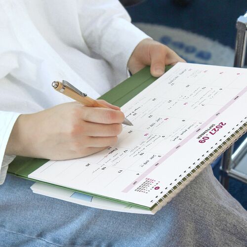 The open calendar rests across a lap with a pen, displaying a practical layout for writing plans on the move.