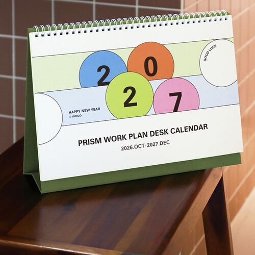 The calendar stands on a wooden desk beside a clock and pen, making its upright desktop format clear.
