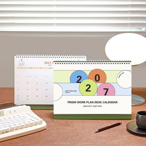 Set on a wooden desk with a keyboard and coffee, the calendar adds a clear planning point to a daily work area.