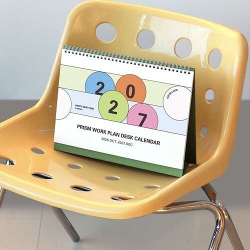 The calendar is displayed on a yellow chair, emphasizing its compact upright design and colorful geometric cover.