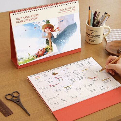 The calendar is angled on a wooden desk beside writing tools, giving a clear view of its upright spiral-bound design.